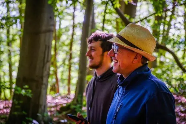 Zwei Männer stehen im Wald und schauen lächelnd in die Ferne